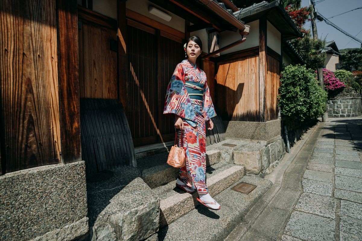 local female teenager girl going out from home walking down stairs to join summer festival wearing colorful kimono under sunshine. elegant japanese woman in traditional dress live old wooden house